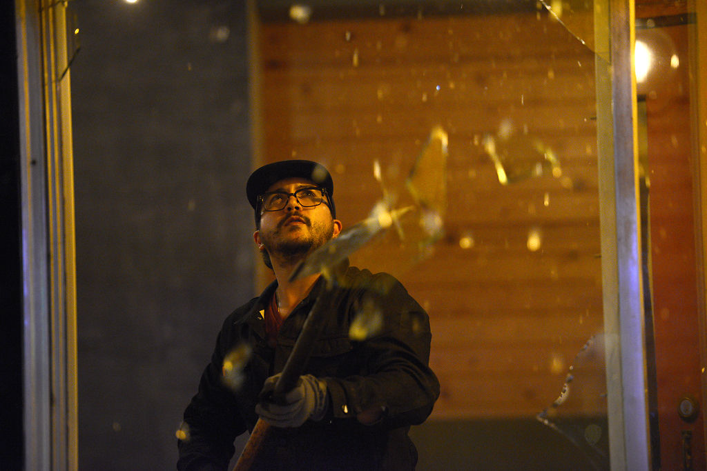 A worker uses a shovel to break out remaining glass from a window